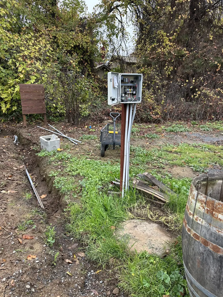 Electrical control enclosure on a post with conduit dropping into a freshly dug trench across a rural Sonoma County yard